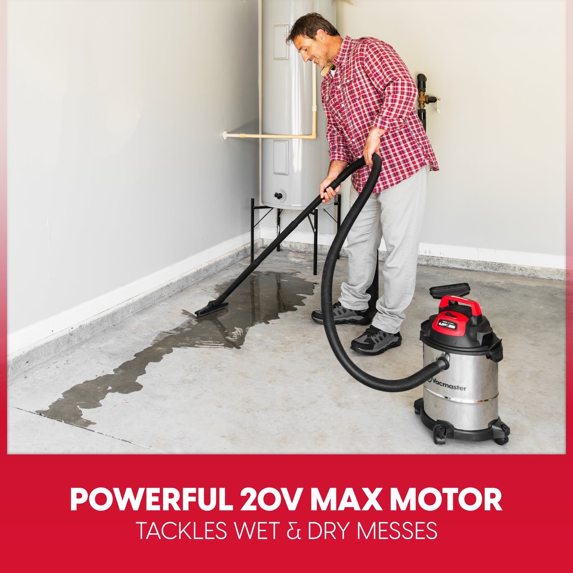 A man in a red plaid shirt and gray pants uses a wet/dry shop vacuum cleaner to clean up water on a concrete floor in a garage. The vacuum is silver with red accents.