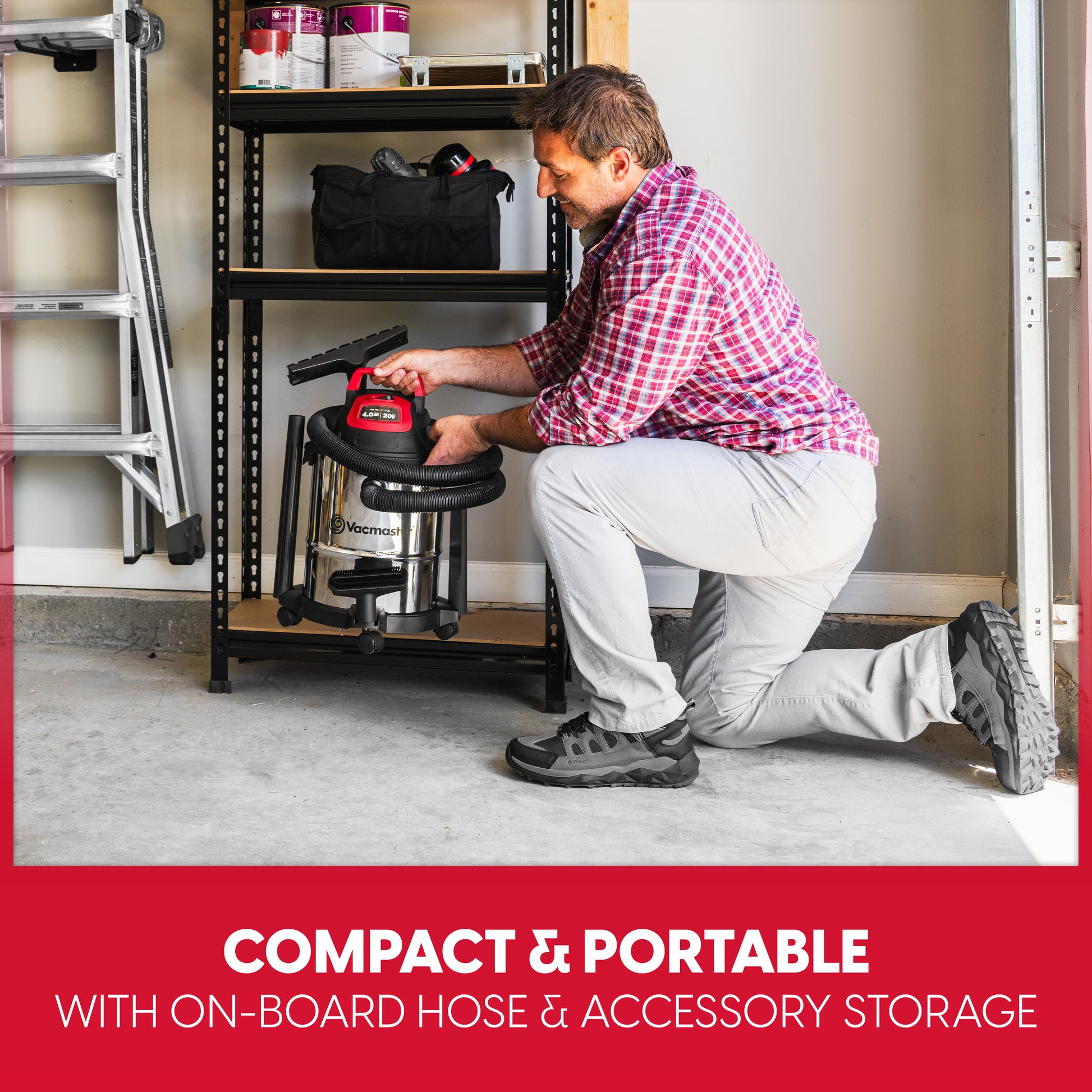 A man in a red and white plaid shirt kneels on a concrete floor in a garage, using a compact wet vacuum cleaner with an on-board hose and accessory storage. A black metal shelving unit stands behind him, and a red banner at the bottom reads 'COMPACT & PORTABLE WITH ON-BORD HOSE & ACCESSORY STORAGE'.