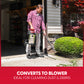 A man in a red plaid shirt and gray pants stands in a garage doorway holding a wet/dry shop vacuum with a long hose attachment, shown clearing dust and debris from a green shrub in a front yard. A red banner at the bottom reads 'CONVERTS TO BLOWER IDEAL FOR CLEARING DUST & DEBRIS'.