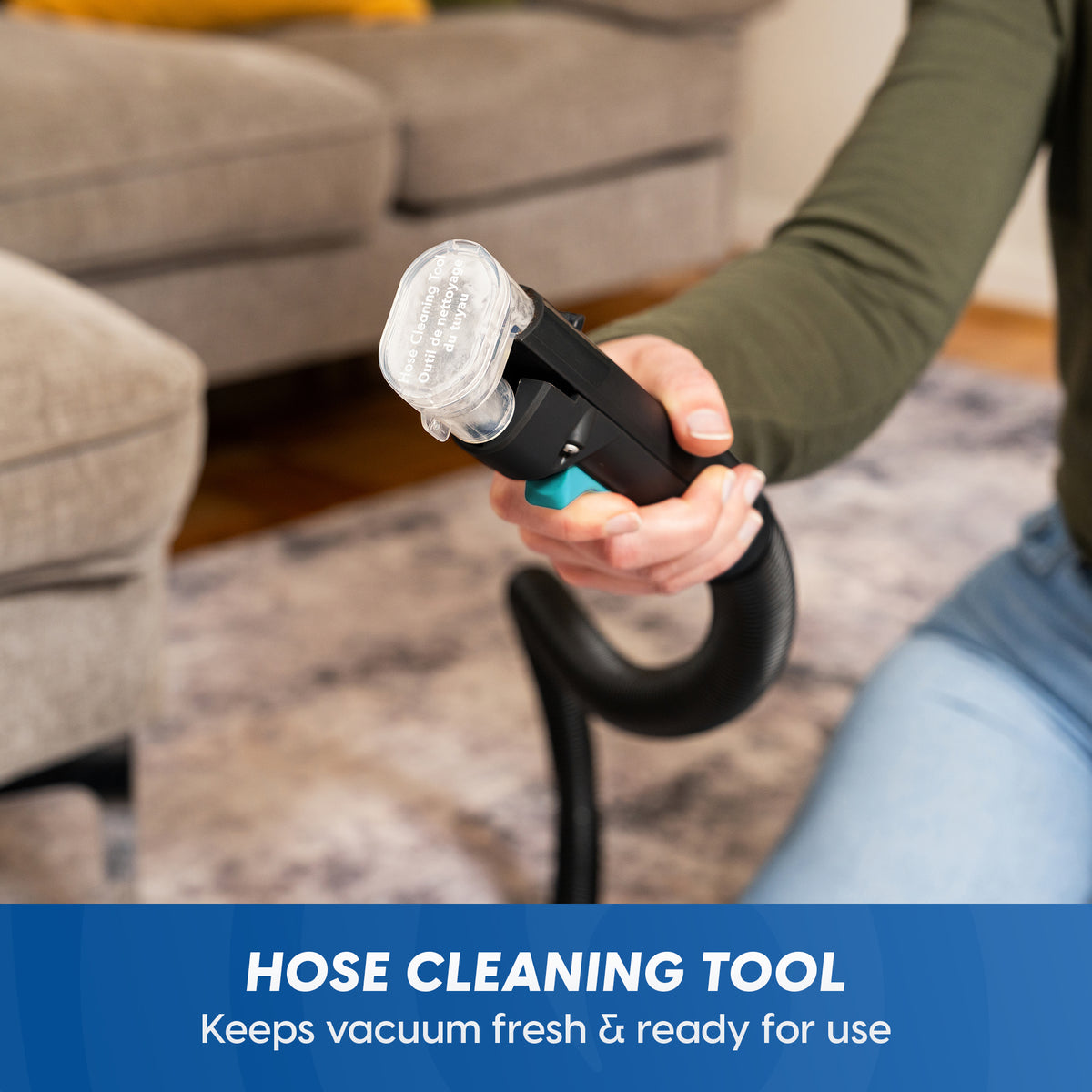 A person in an olive green long-sleeve shirt holds a handheld hose cleaning tool with a clear filter and black hose attachment in a living room setting. A blue banner at the bottom reads 'HOSE CLEANING TOOL Keeps vacuum fresh & ready for use'.