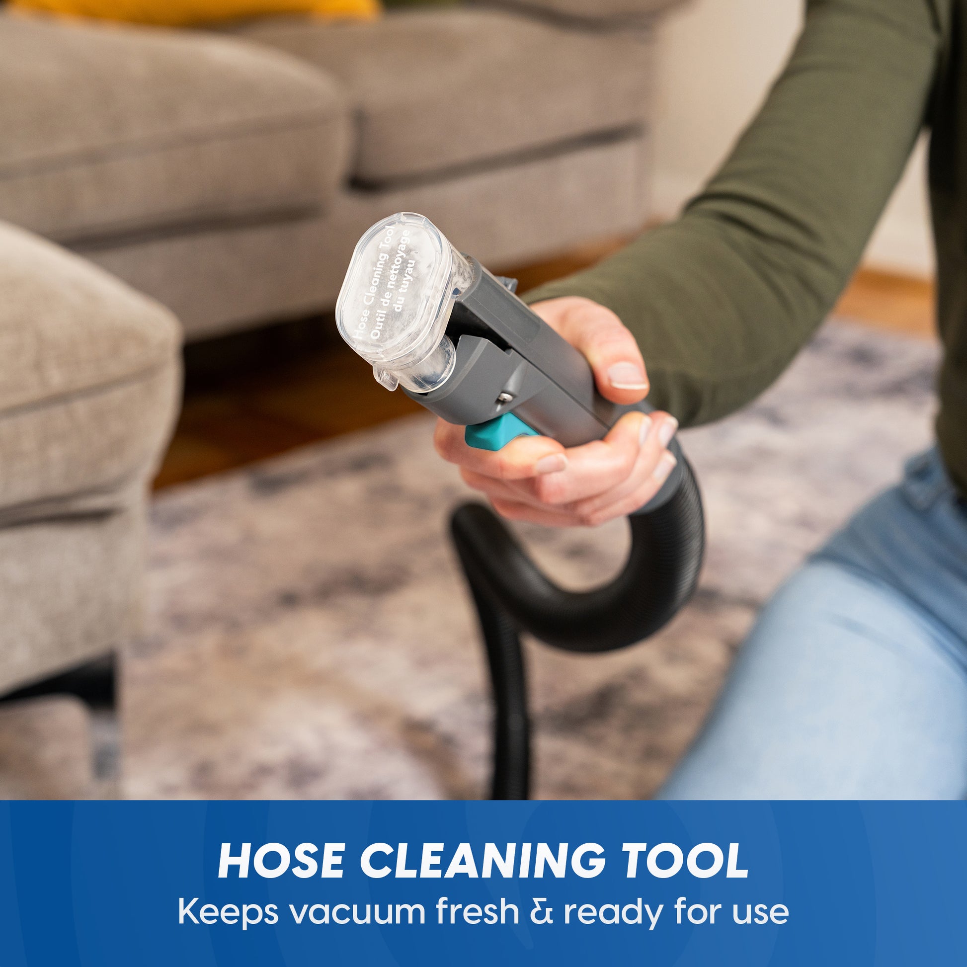 A person holds a handheld hose cleaning tool with a clear nozzle and black hose in a living room setting. A blue banner at the bottom reads 'HOSE CLEANING TOOL Keeps vacuum fresh & ready for use'.