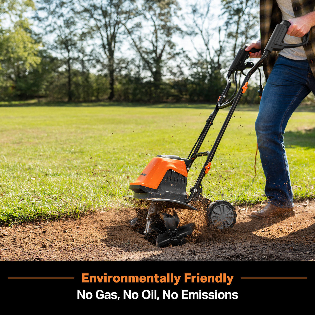 Person using a corded electric tiller on a grassy area with trees in the background.
