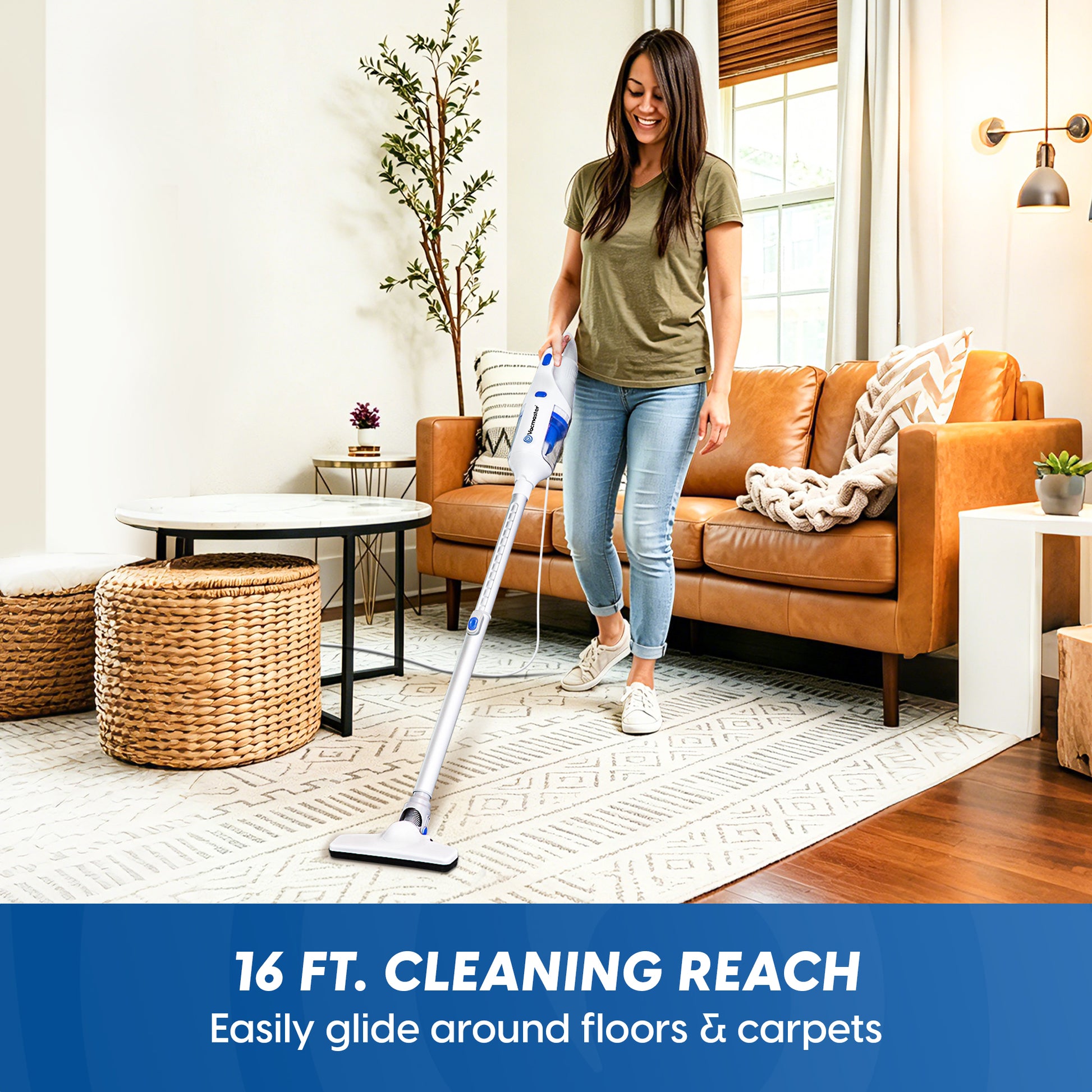 A woman in a living room using a cordless stick vacuum cleaner on a patterned area rug. The vacuum has a white body with blue and silver accents.