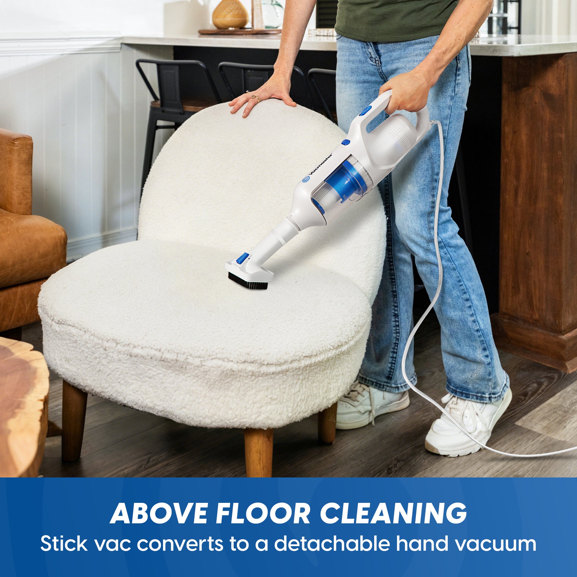 A person using a white and blue stick vacuum cleaner to clean a white boucle armchair in a home setting, with text at the bottom reading 'ABOVE FLOOR CLEANING Stick vac converts to a detachable hand vacuum'.