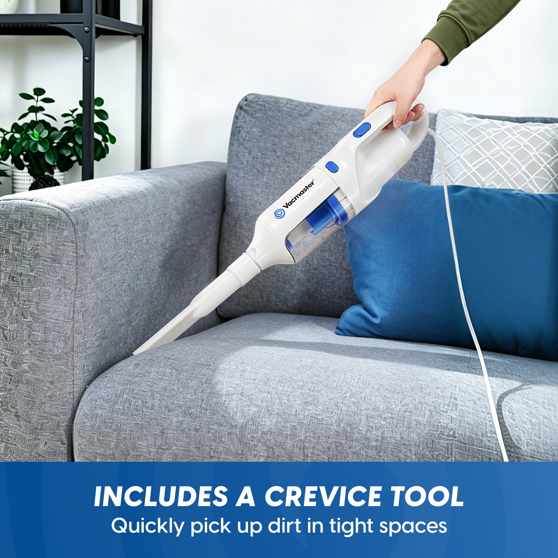 A handheld cordless vacuum cleaner being used on a gray fabric sofa, with a person's hand and arm visible holding it. The vacuum is white with blue accents, and the scene includes a blue throw pillow and a text banner at the bottom that reads 'INCLUDES A CREVICE TOOL Quickly pick up dirt in tight spaces.